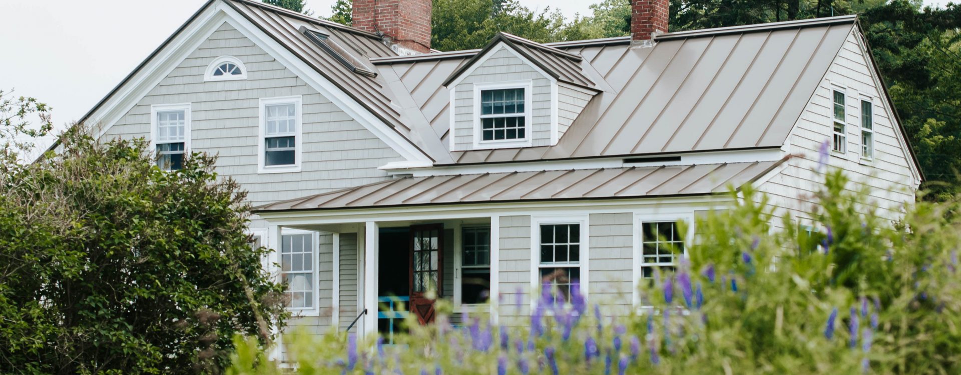 Traditional house with cedar shingles against a backdrop of wildflowers and mature trees.