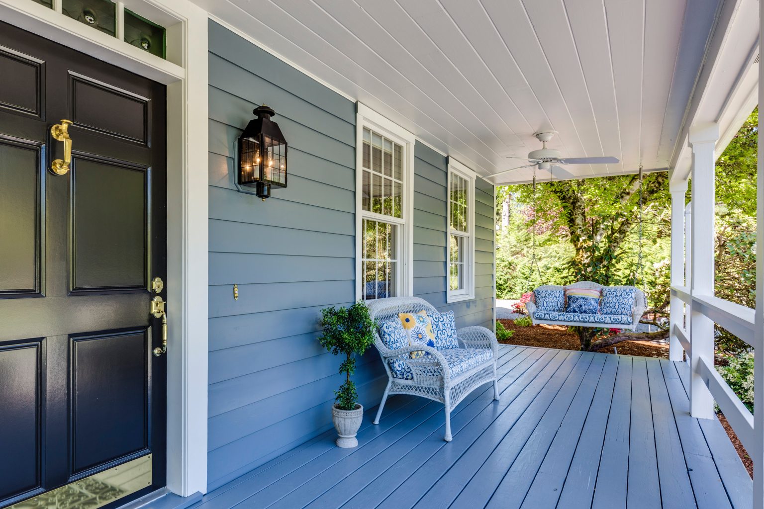 Cozy front porch with wicker furniture and blue cushions on a suburban home.