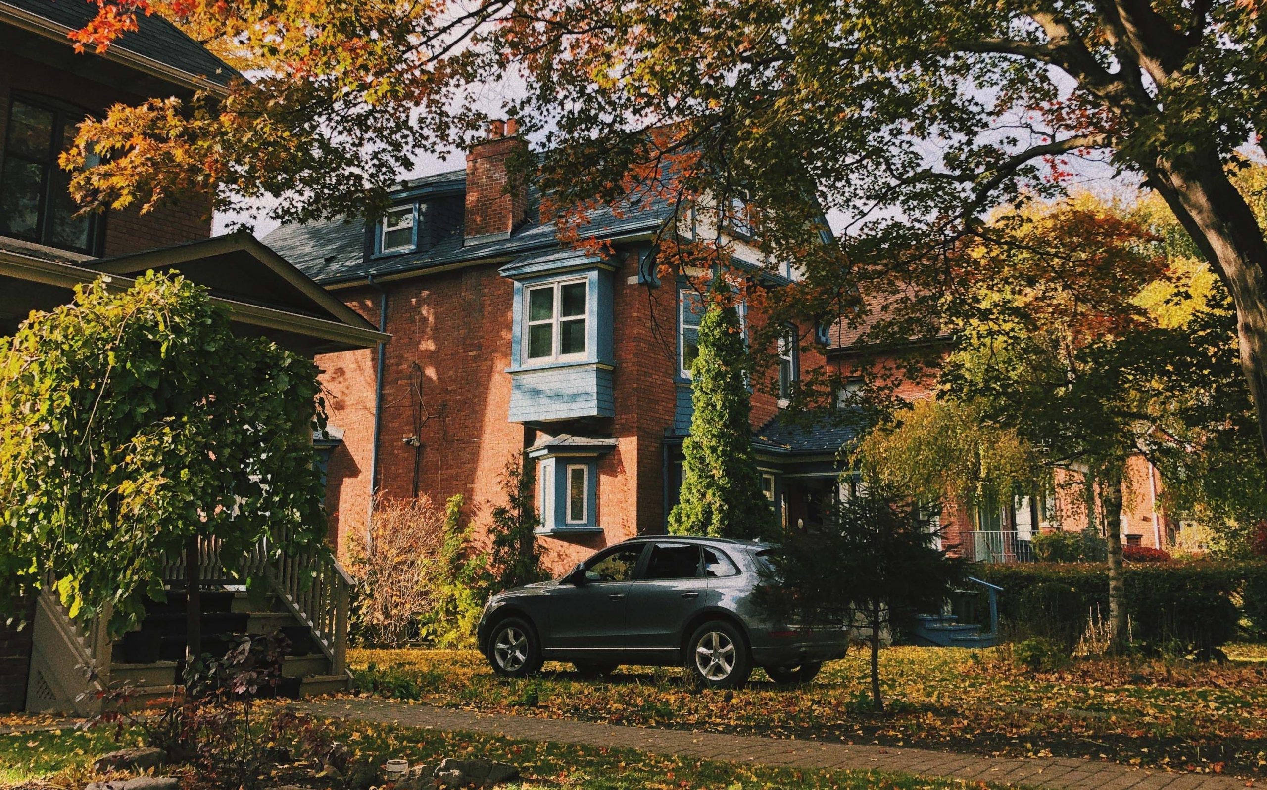 A car parked on the driveway of a classic brick house with autumn foliage