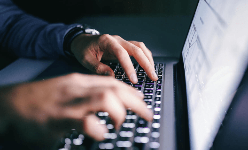 Hands typing on a laptop keyboard in a dark setting.