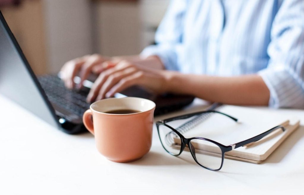 Close-up of hands typing on a laptop, planning for franchise success, with coffee and glasses nearby.
