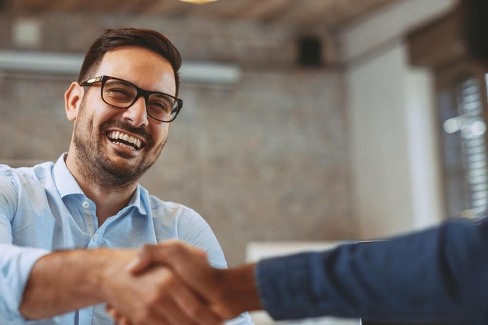 A cheerful man shaking hands with another individual in a business setting.