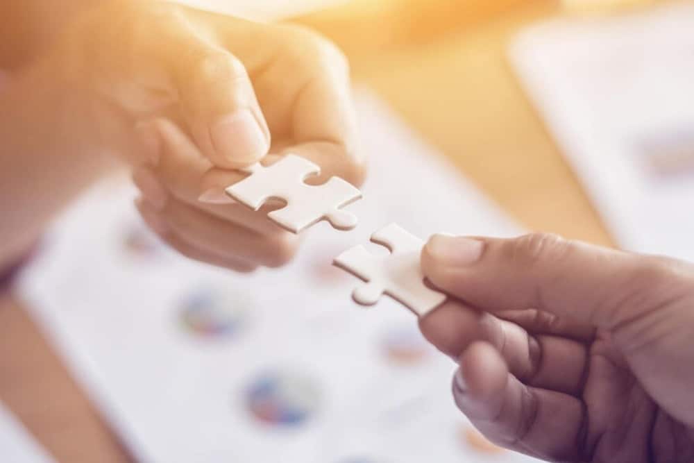 Two hands joining puzzle pieces together over a business strategy document.