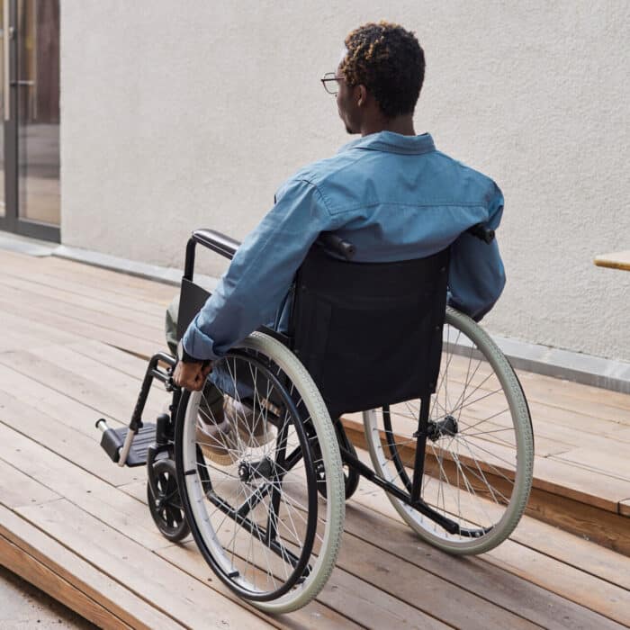 Man in wheelchair using exterior wooden accessibility ramp at home entrance