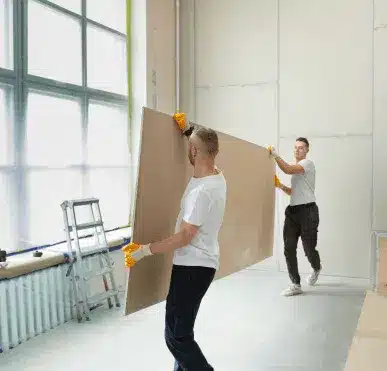 Two contractors carrying a wall panel while completing repairs and finishing home updates
