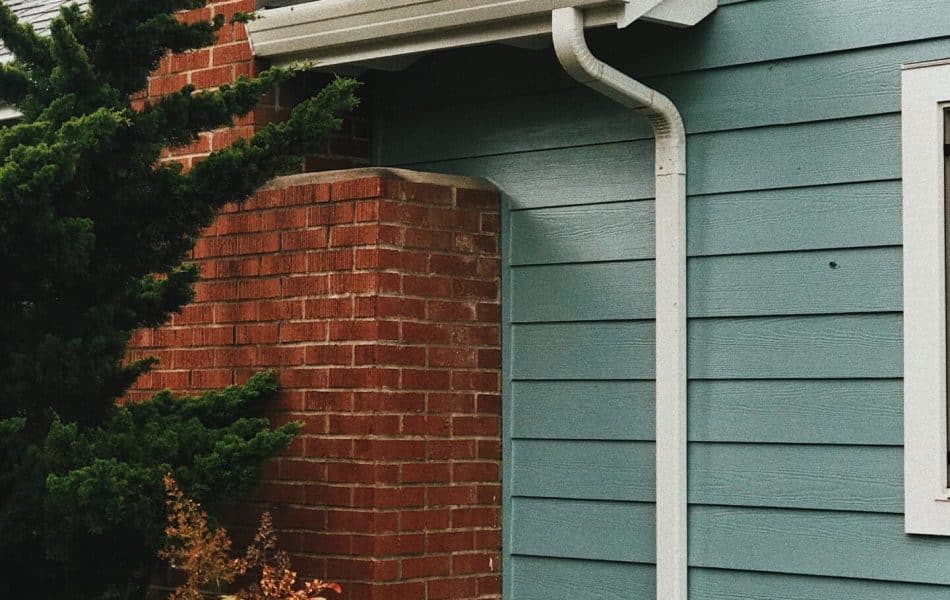 Close-up of a house's corner showing a downspout against brickwork and blue siding.